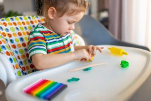 Bébé joue debout devant une table d’activité colorée adaptée à son âge.