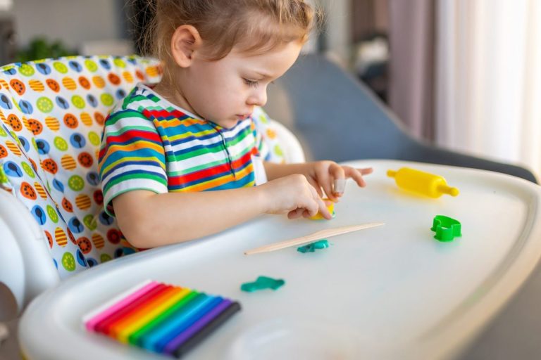 Bébé joue debout devant une table d’activité colorée adaptée à son âge.